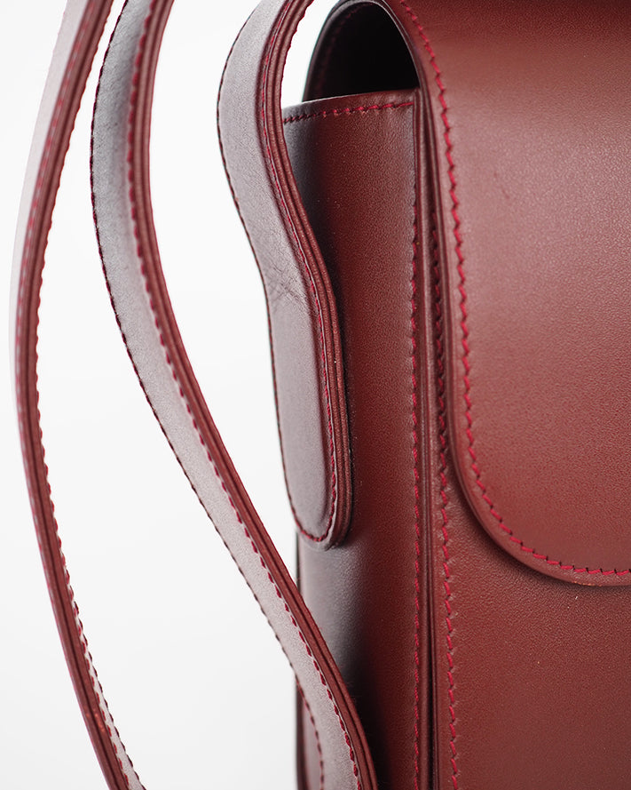 Oxblood leather flap front bag with embossed leather closure and long adjustable buckle strap.