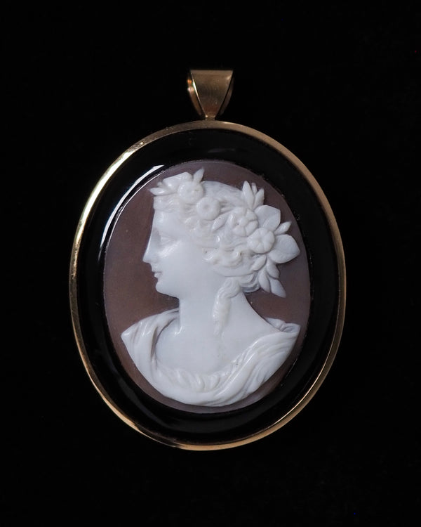 Exquisite vintage shell cameo with onyx surround and set in 14k gold. This is a rare left-facing profile cameo with delicately hand-carved botanical wreath crown - dating to approximately the early mid century. Piece features retractible bail that leaves pendant flush when being worn as brooch.