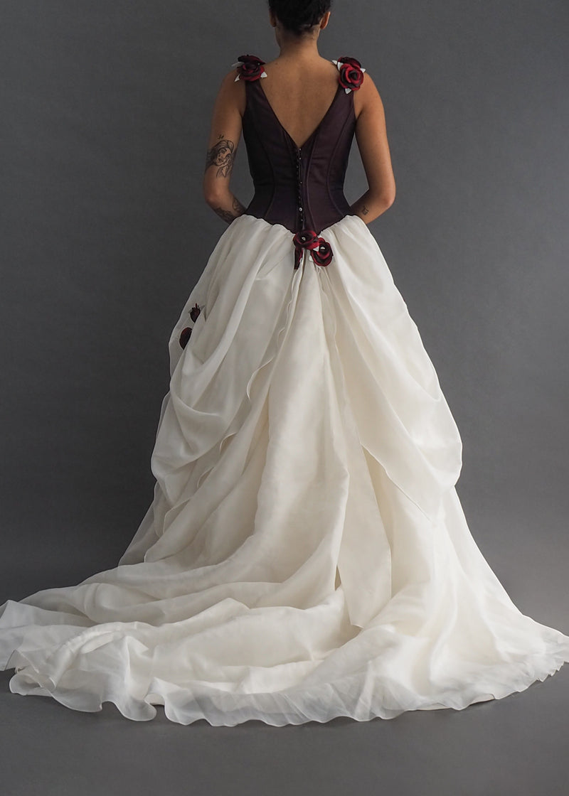 IAN STUART - Snow White bridal gown Iridescent burgundy corseted bodice, pointing to a strategically gathered, off-white ballgown skirt, trussed up with burgundy rosettes on flounces and straps