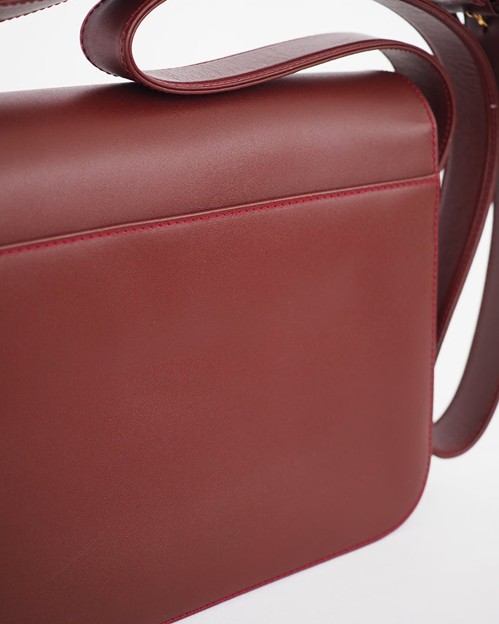 Oxblood leather flap front bag with embossed leather closure and long adjustable buckle strap.