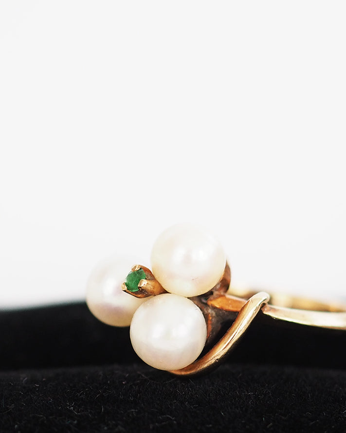 10k gold knotted ring set with three cultured pearls and an emerald chip.